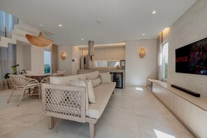 Ein modernes Wohnzimmer mit Sofa, Essbereich, Küche und einem großen Fernsehbildschirm.