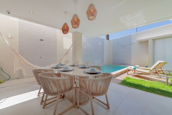 A modern outdoor dining area with a pool, wicker furniture, and a clear view of the sky.
