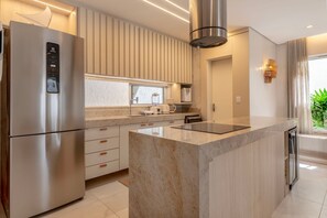 A modern kitchen with a stainless steel refrigerator, a built-in oven, and a central island with a glass top.