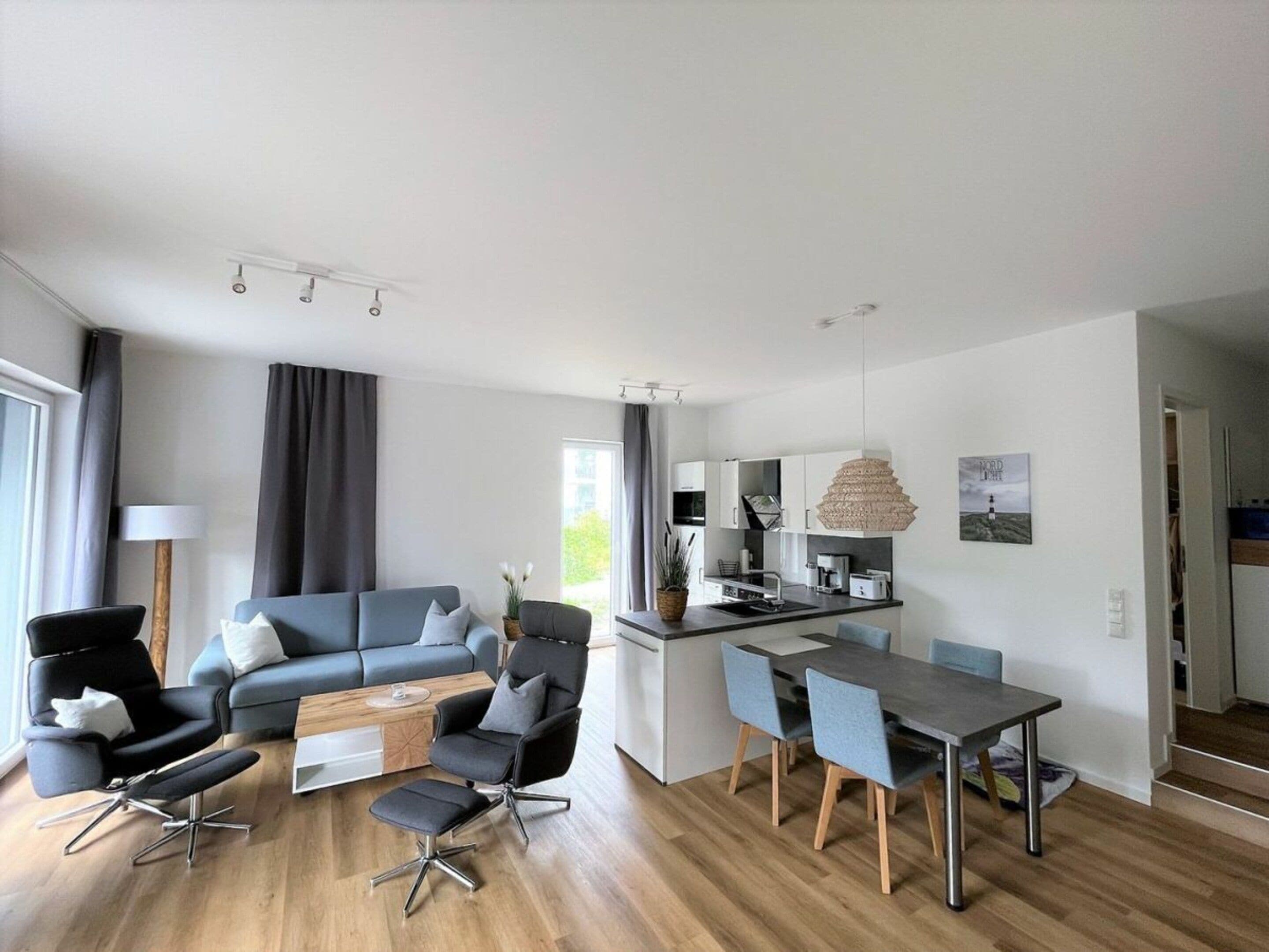 A modern living room with a sofa, chairs, a dining table, and a kitchen area with a sink and cabinets.