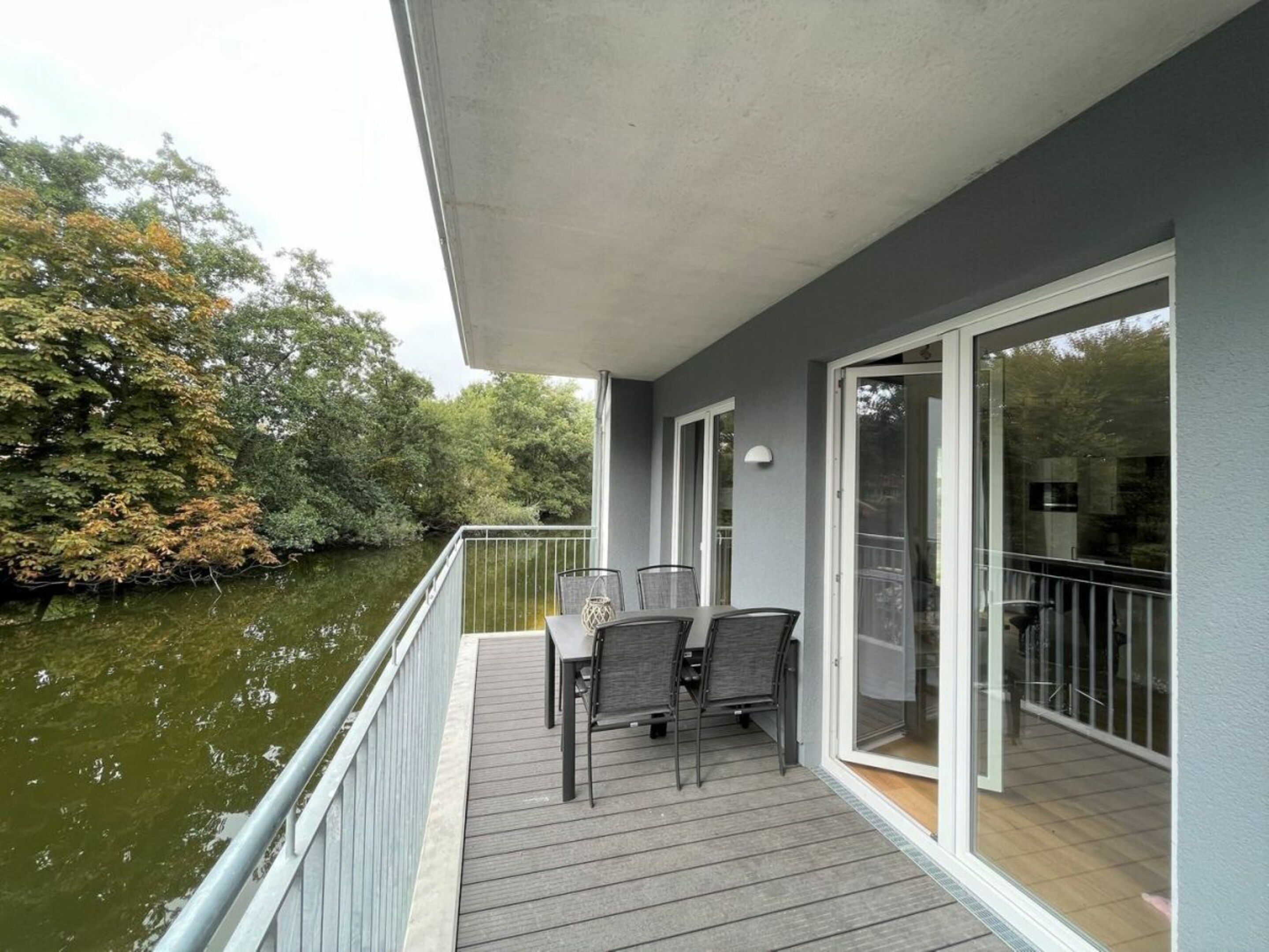 A balcony with a table and chairs overlooking a body of water, with a railing and a door leading to an interior space.