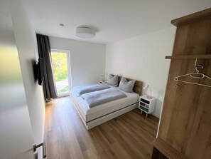 A bedroom with a bed, bedside tables, a wardrobe, and a window with curtains. - 49.0.s Waterkant (Wangerland)