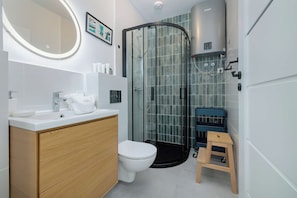A modern bathroom with a glass shower enclosure, a white toilet, and a wooden vanity with a mirror. - Rusinowo | Bosmańska 2 | Cosy Apartment | Balcony | Close to the sea (Rusinowo)