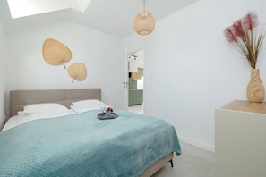 A bedroom with a bed, a bedside table, a hanging light fixture, and a wall-mounted decorative item. - Rusinowo | Bosmańska 2 | Cosy Apartment | Balcony | Close to the sea (Rusinowo)