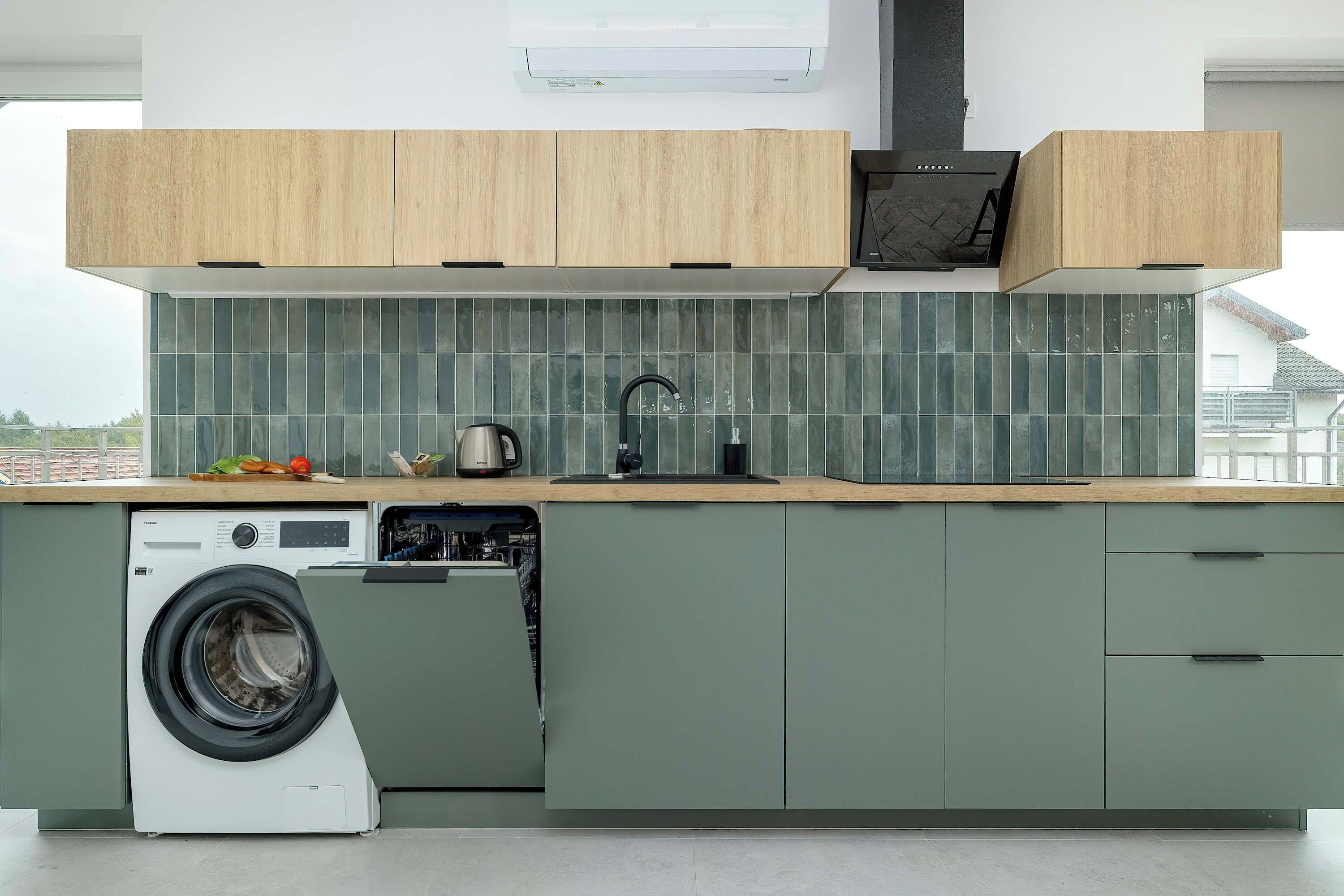 Une cuisine moderne équipée d’un lave-linge et d’un sèche-linge intégrés, d’une grande fenêtre et offrant une vue sur la ville.