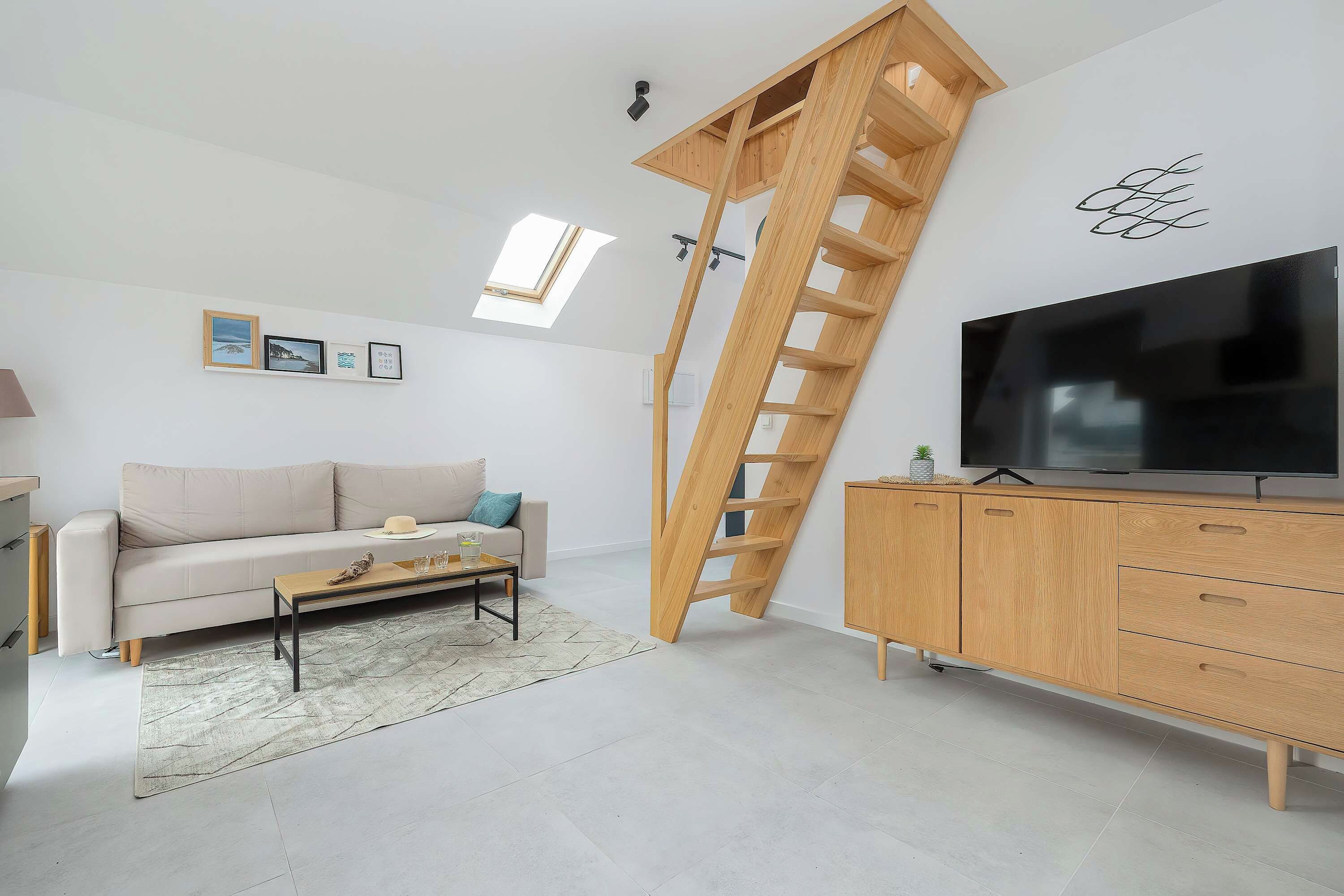 A modern living room with a sofa, coffee table, TV, wooden ladder, and artwork on the wall.