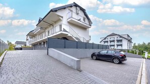Un moderno edificio residencial de varios pisos con balcones, un camino de entrada con puerta de acceso y un área de entrada pavimentada.