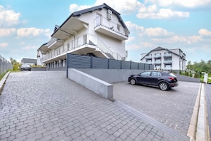 A modern multi-story residential building with balconies, a gated driveway, and a paved entrance area. - Rusinowo | Bosmańska 2 | Cosy Apartment | Balcony | Close to the sea (Rusinowo)