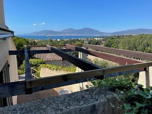 A terrace with a view of the sea and mountains, a wooden railing, and a building with a tiled roof. - Bright house in Porticcio for 6 people (Grosseto-Prugna)