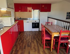 A compact kitchen with red cabinets, a white refrigerator, a microwave, a stove, and a dining table with red chairs. - Bright house in Porticcio for 6 people (Grosseto-Prugna)