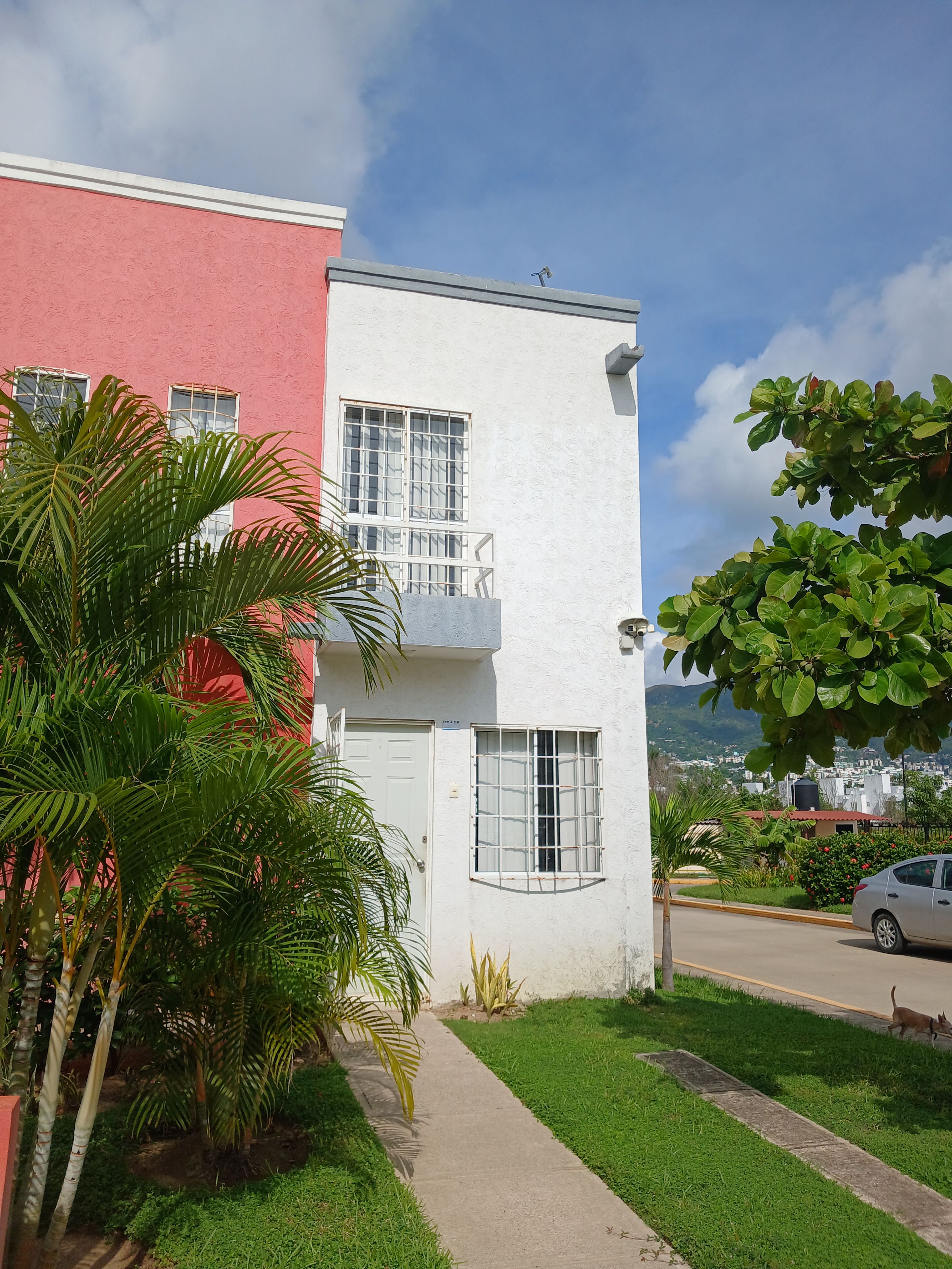 A two-story building with a red and white facade, a visible door, and a window with a metal grid.