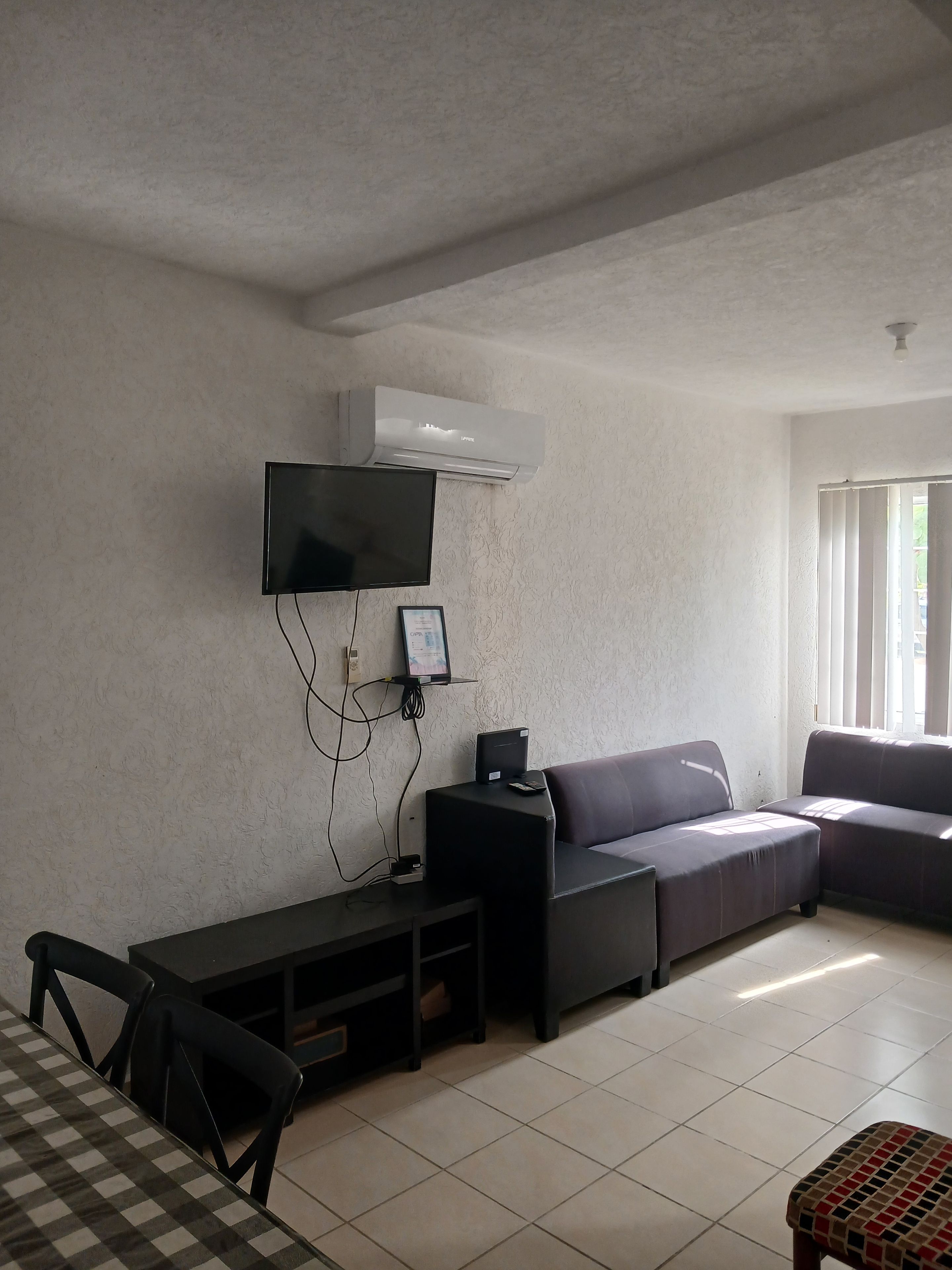Un salon équipé d’un téléviseur à écran plat, d’un appareil de climatisation, d’un canapé et d’une table à manger avec des chaises.