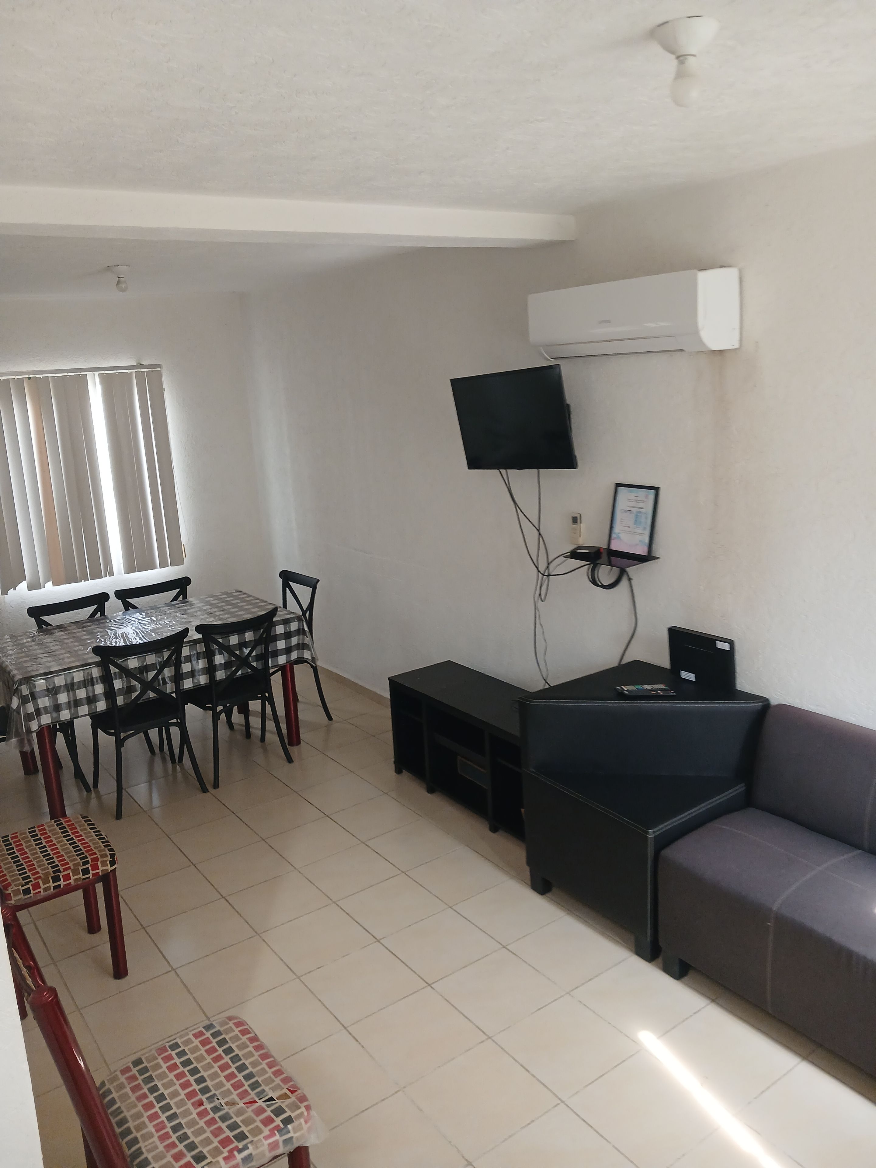 A living room with a dining area, a flat-screen TV mounted on the wall, and a sofa.