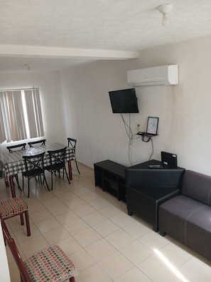 Una sala de estar con comedor, un televisor de pantalla plana en la pared y un sofá.