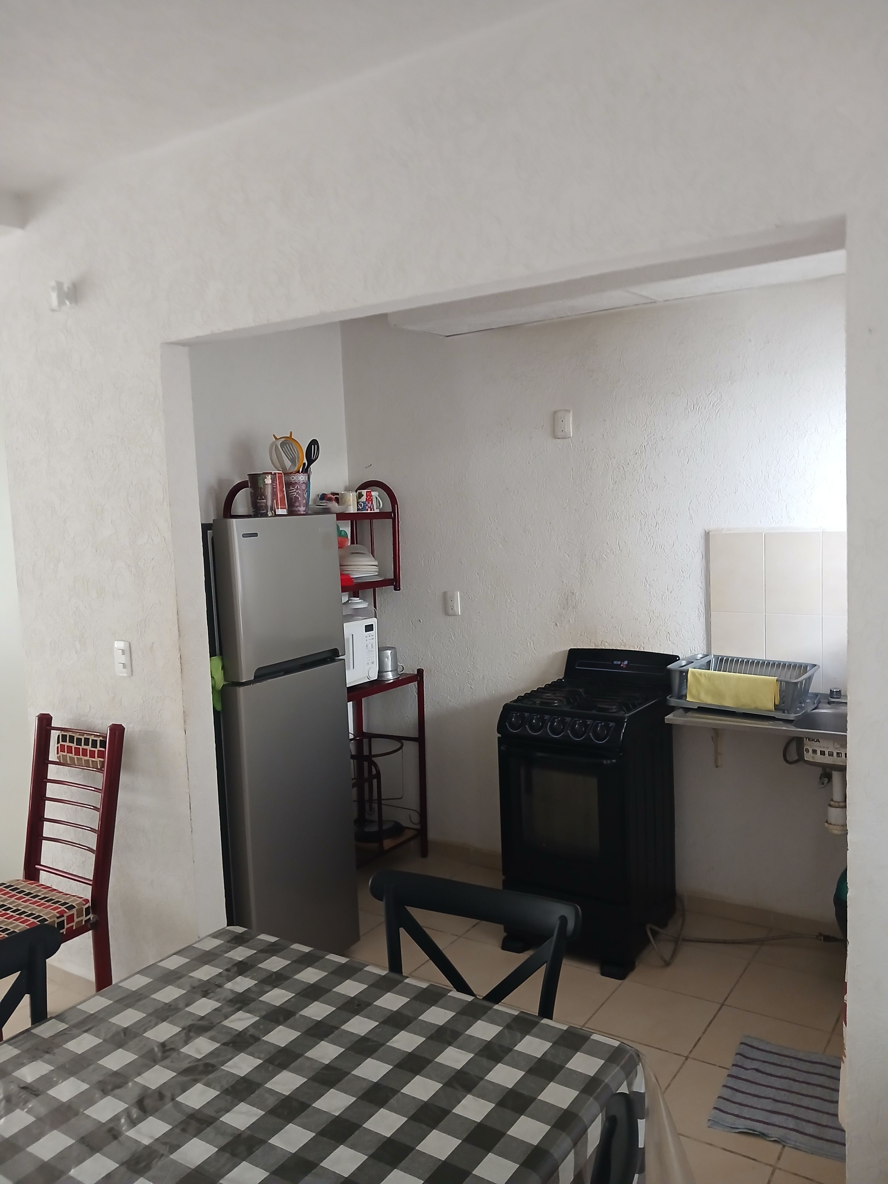 Een functionele keuken met een koelkast, magnetron, kookplaat en een eettafeltje met stoelen.