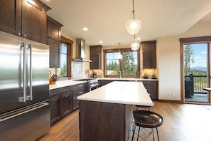 A modern kitchen with dark wood cabinets, stainless steel appliances, and a large island with bar stools. - Eagle Ridge Lookout: Private Hot Tub, Mountain Views (Breckenridge)