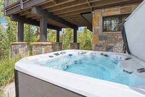 Ein Whirlpool mit Steinverkleidung, unter einer hölzernen Pergola gelegen, umgeben von viel Grün.