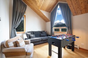 Un salon confortable avec un canapé, une table de baby-foot et une vue sur les montagnes grâce à de grandes fenêtres.
