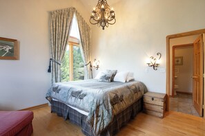 Ein Schlafzimmer mit Bett, Vorhängen, einer Chandelier, Wandleuchten, einem Fenster mit Blick und einer Holztür.