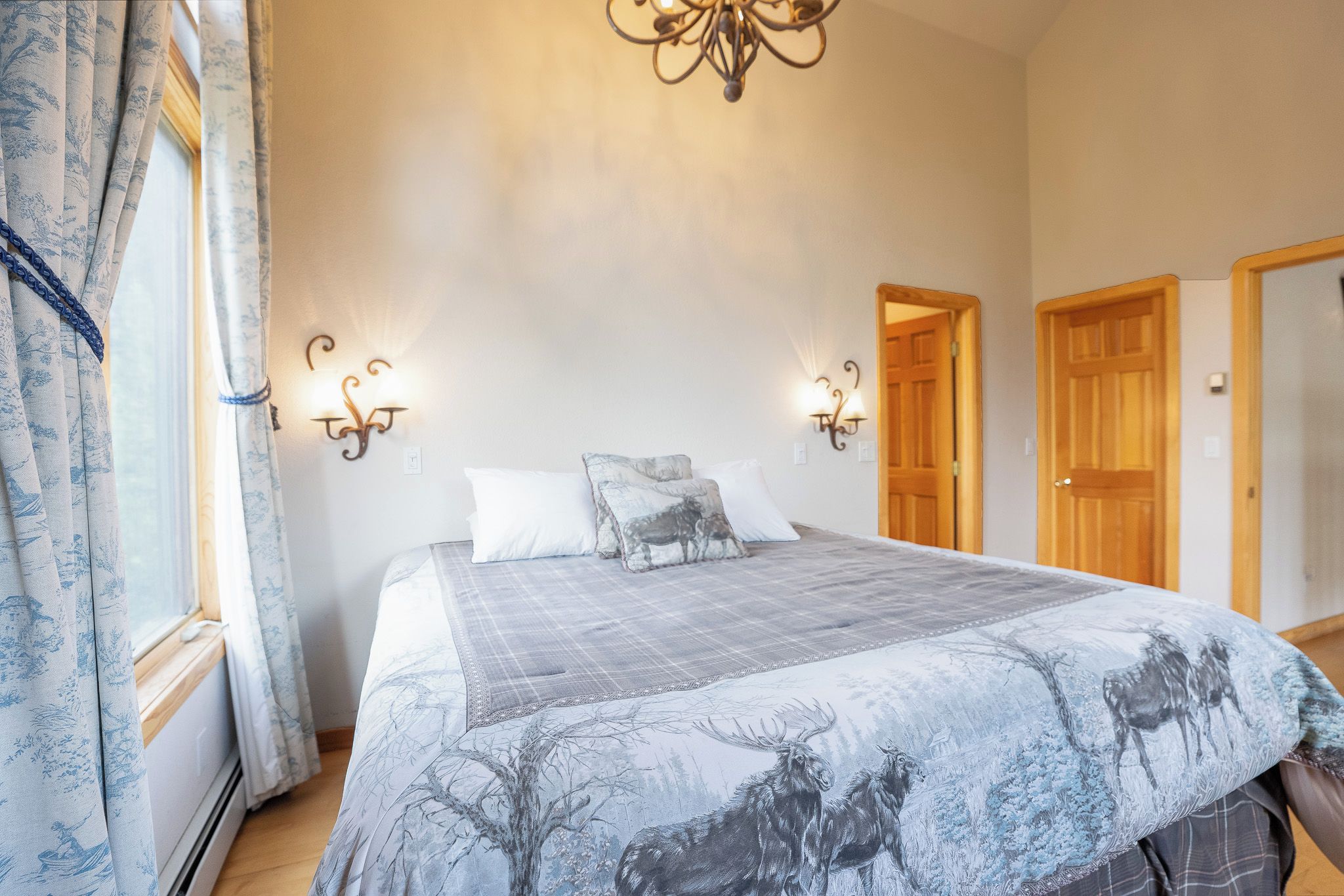 A bedroom with a bed, two wall sconces, a chandelier, and a door.