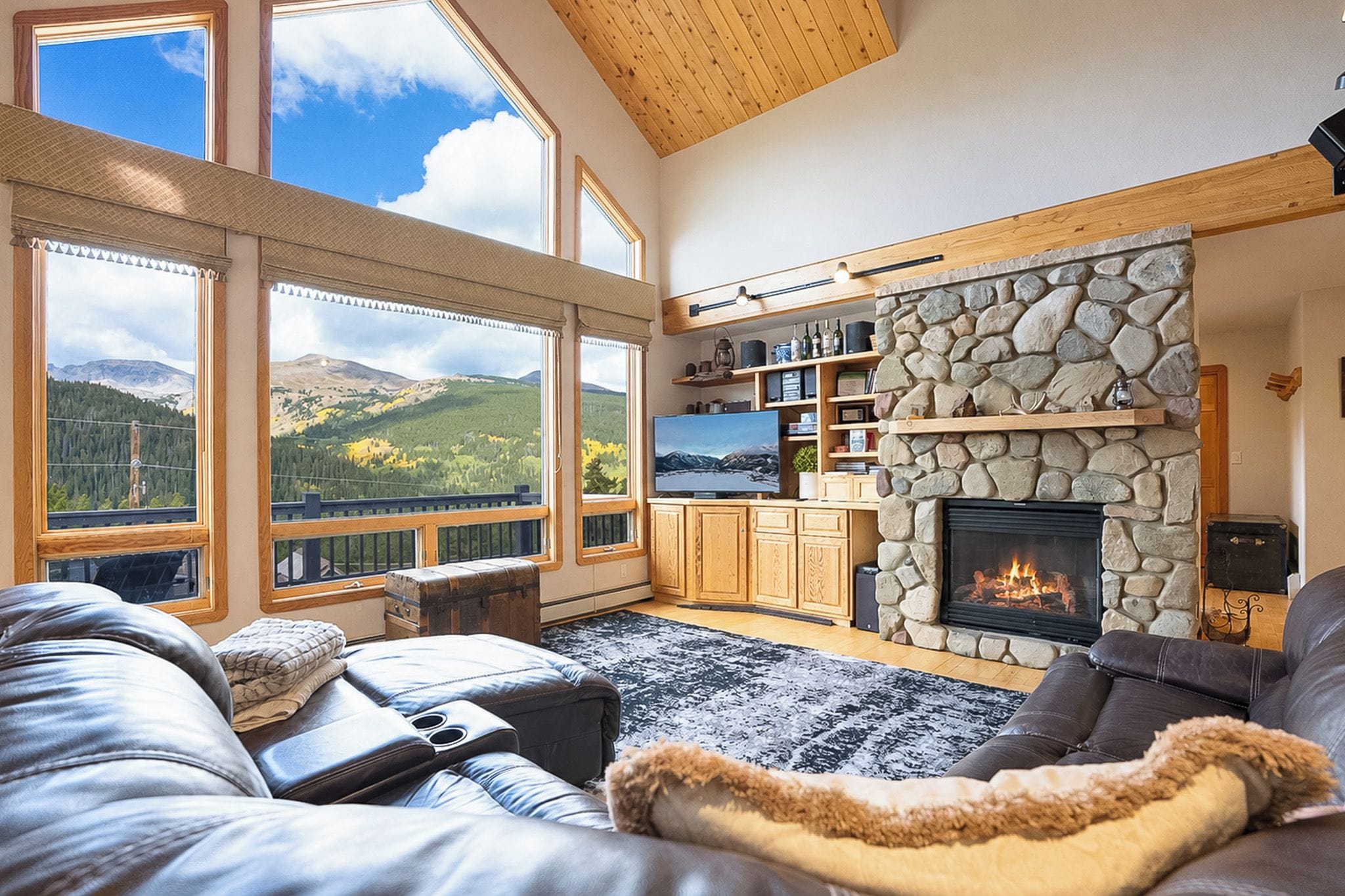 A spacious living room with a stone fireplace, large windows offering mountain views, and a cozy seating area.