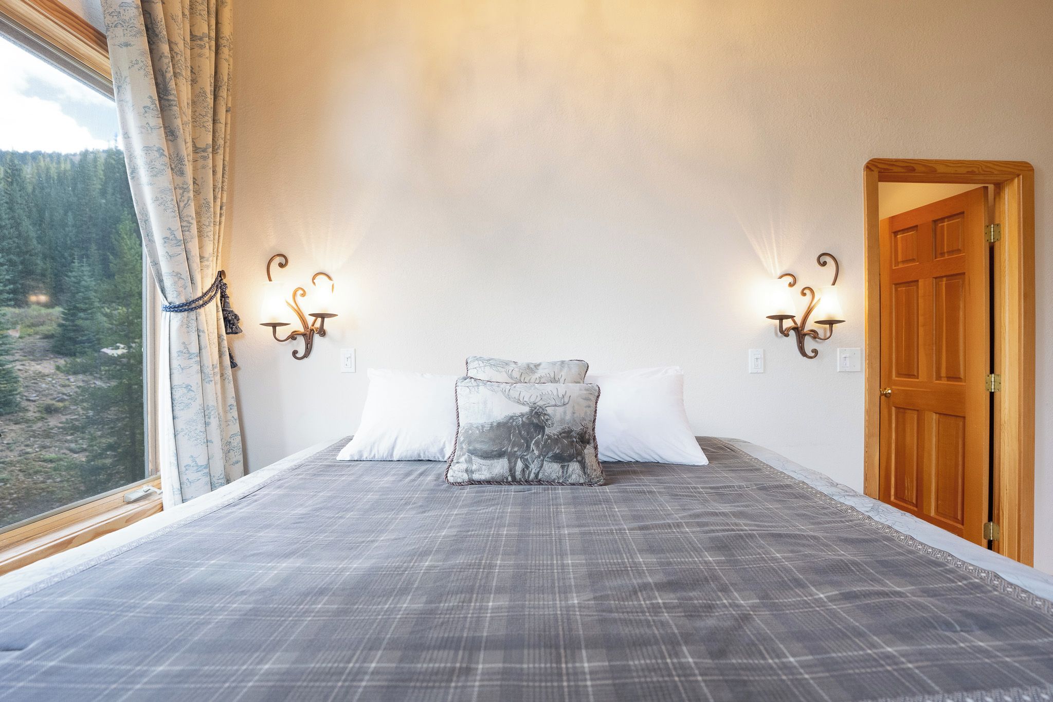 Une chambre à coucher avec une couvre-lit à carreaux, un coussin orné d’un motif d’élan et deux appliques murales.