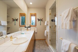 Une salle de bain avec deux vasques, une douche et une fenêtre donnant sur les arbres.
