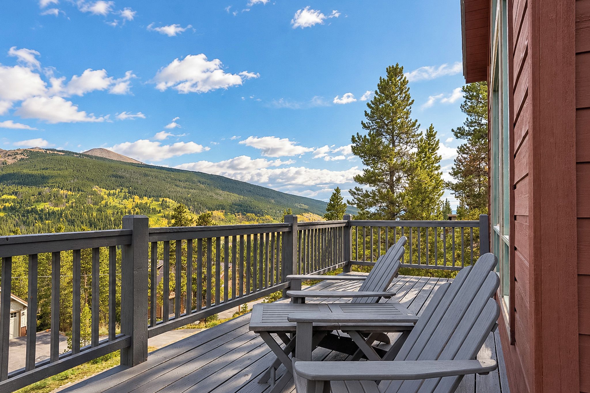 A wooden deck with a table and chairs, overlooking a mountainous landscape.