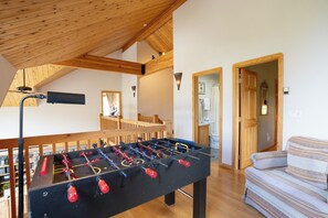 Ein Zimmer mit Tischfußballtisch, Holzbalken, einer Couch und einem durch eine offene Tür einsehbaren Badezimmer.