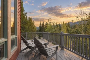 Une terrasse en bois avec deux fauteuils Adirondack, une porte vitrée et une vue sur les arbres et les montagnes.