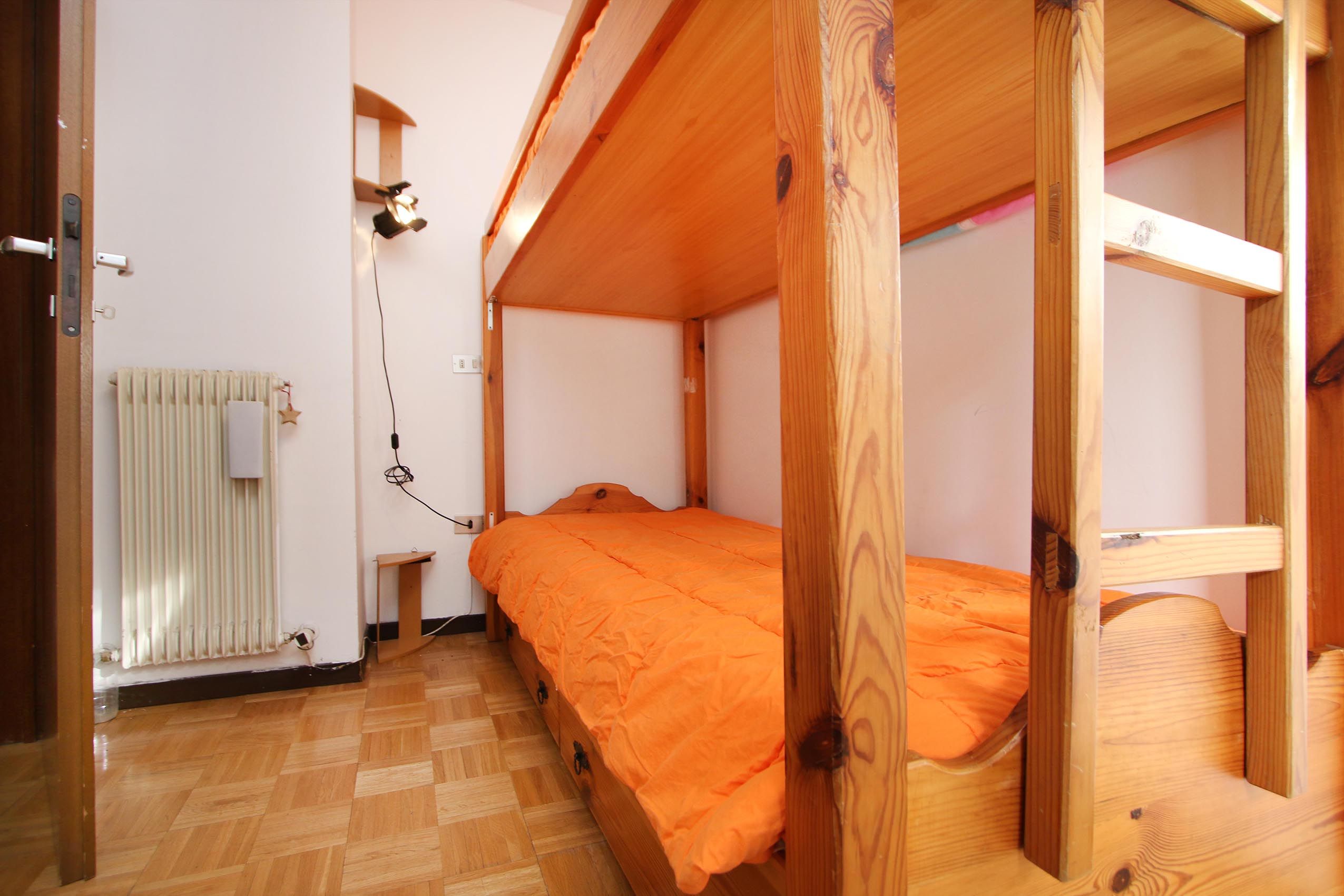 Habitació amb literes, sòl de fusta, radiador i taula petita.