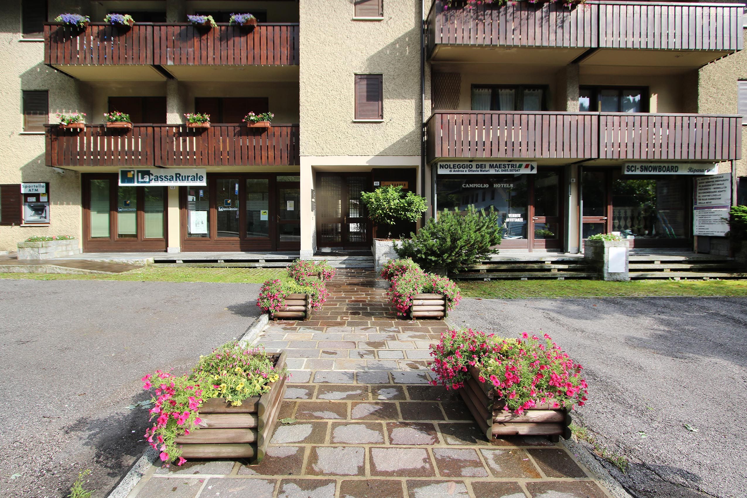 Un hotel amb entrada empedrada de pedra, jardineres de fusta amb flors i balcons amb baranes de fusta.