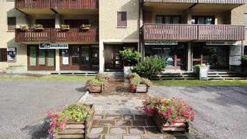 Un hotel amb entrada empedrada de pedra, jardineres de fusta amb flors i balcons amb baranes de fusta.
