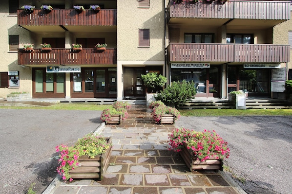 Un hotel amb entrada empedrada de pedra, jardineres de fusta amb flors i balcons amb baranes de fusta.