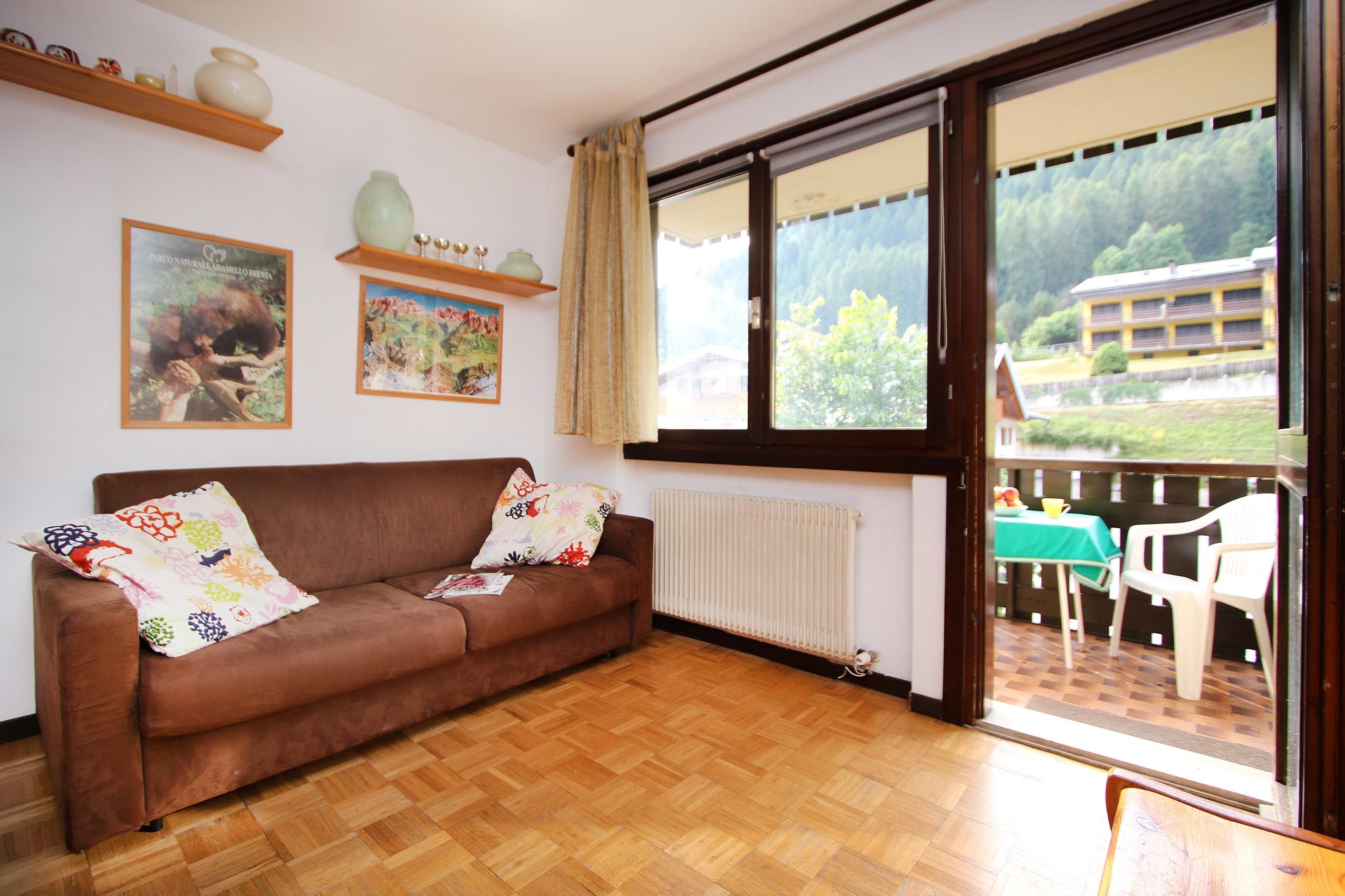Un salon chaleureux avec un canapé marron, un radiateur et une grande fenêtre donnant sur un immeuble et des arbres.