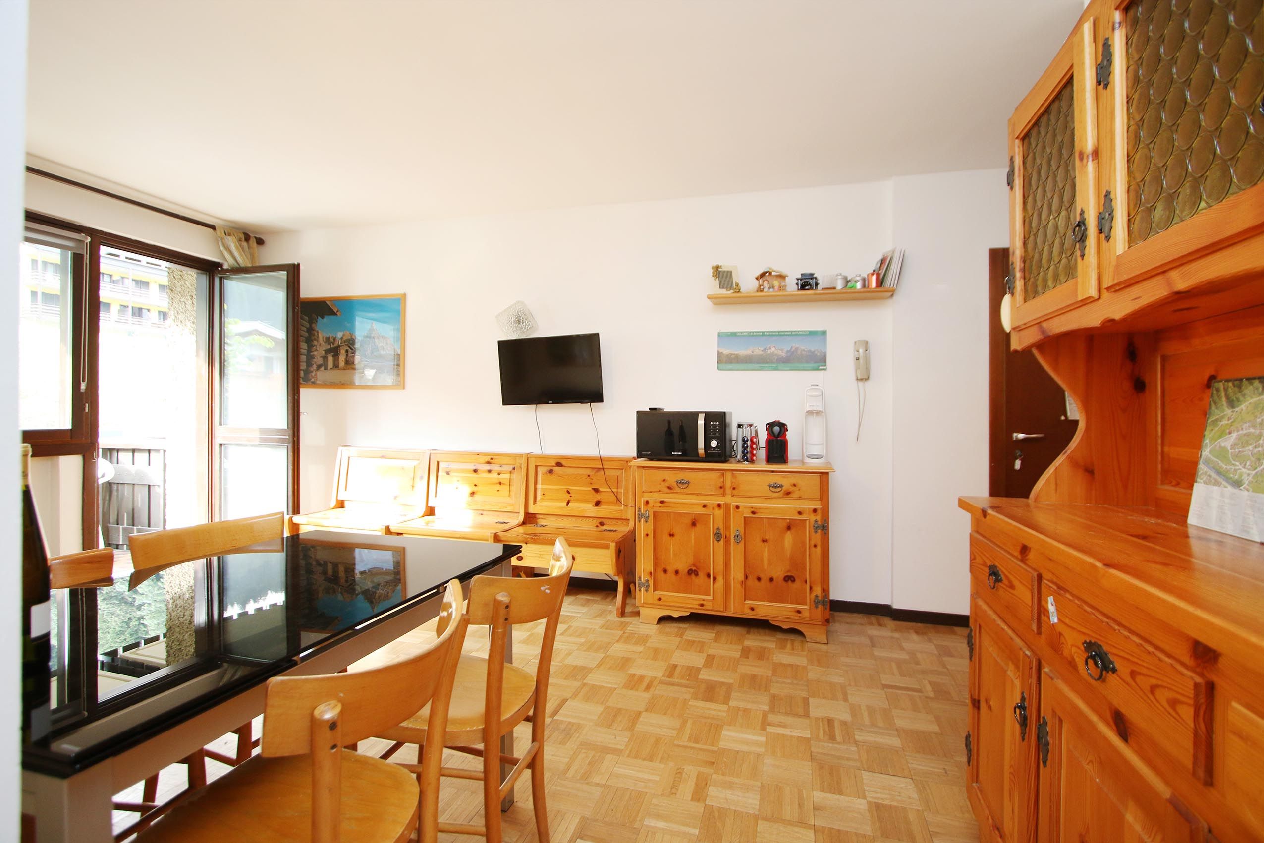 Eine kleine Küche mit Esstisch, Stühlen, Holzschränken, einem Fernseher und einem Fenster.