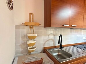 A kitchen with wooden cabinets, a stainless steel sink, and a hanging rack with woven baskets. - Coralia 29, apartment in the historic center of Alghero (Alghero)
