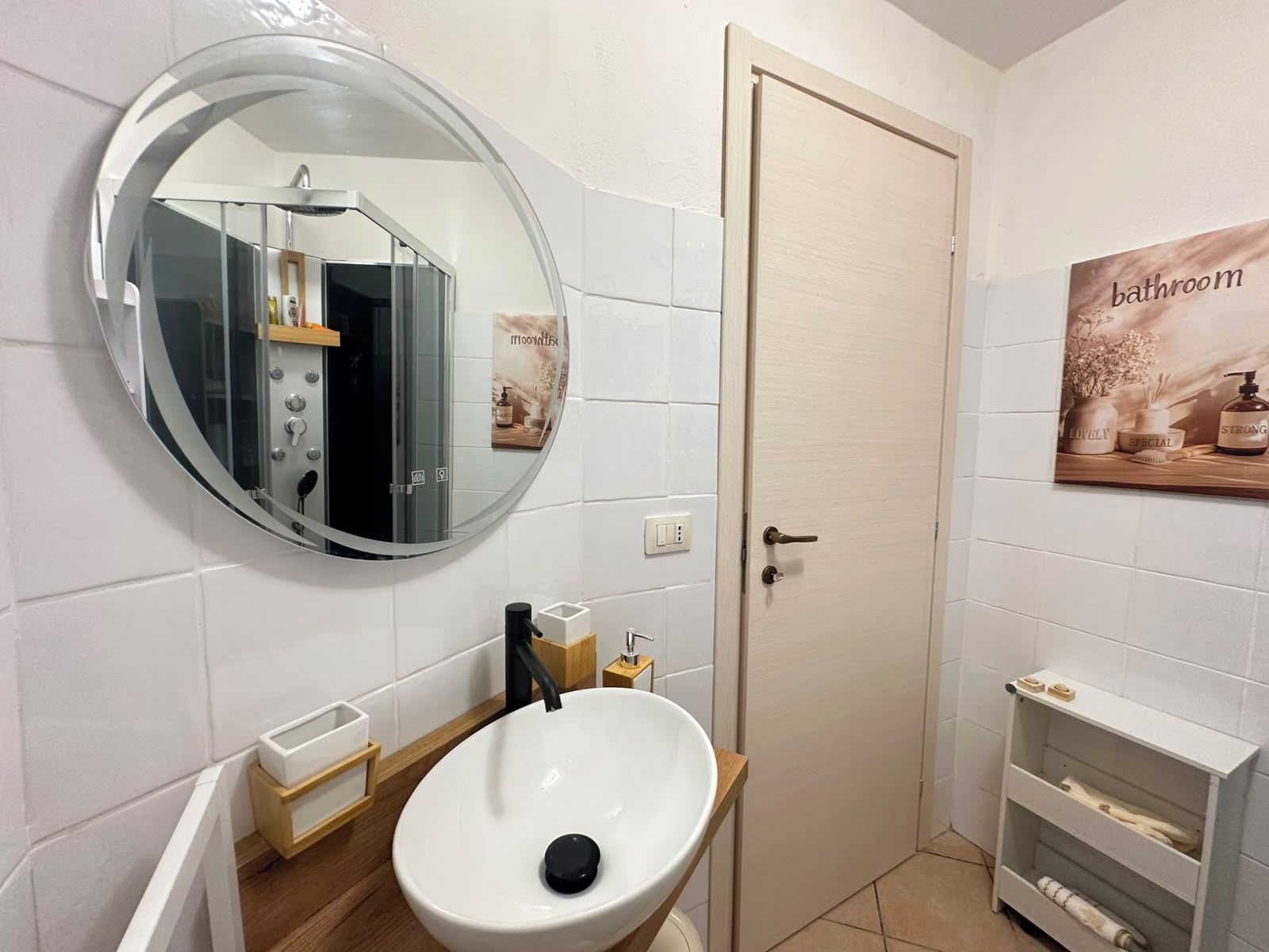A bathroom with a round mirror, a white sink, a door, and a shelf with toiletries.