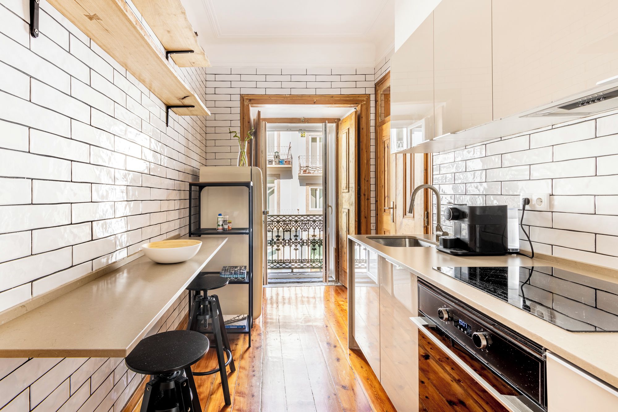 A narrow kitchen with white tiled walls, a wooden countertop, a coffee machine, and a stove.