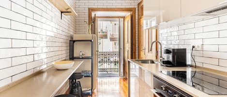 A narrow kitchen with white tiled walls, a wooden countertop, a coffee machine, and a stove.