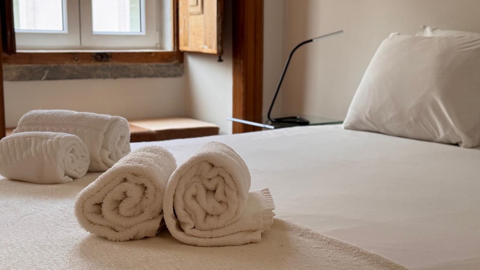 A neatly made bed with rolled white towels and a white pillow.