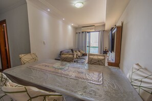 A hotel room with a bed, a table with a glass top, a sofa, and a window with curtains. - Apartment with BBQ 350m from Guilhermina Beach (Praia Grande)