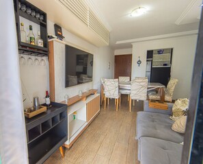 Ein Wohnzimmer mit Flachbildfernseher, einem Esstisch mit Stühlen, einer Couch und einer Küchenzeile inklusive Kühlschrank.