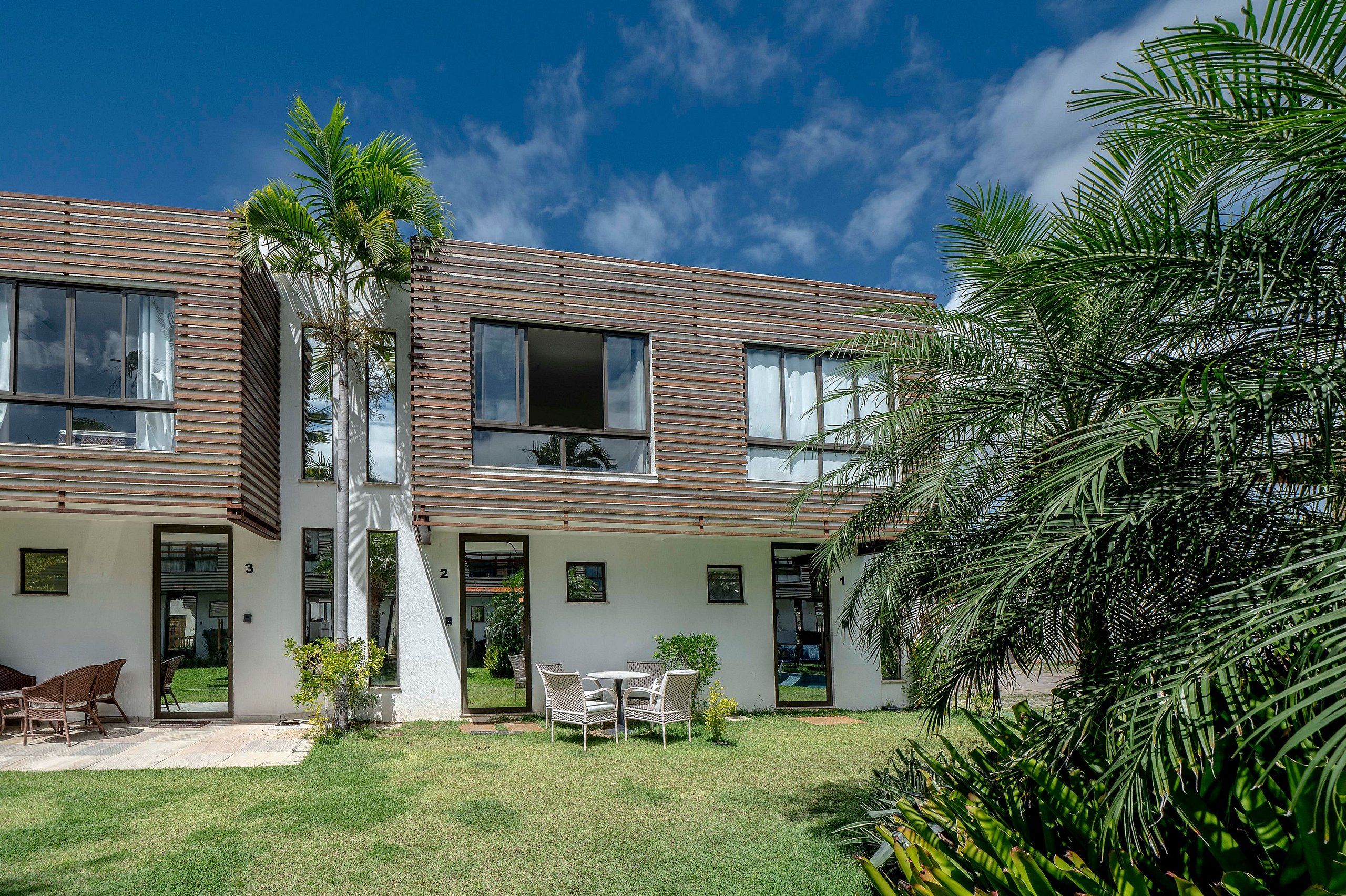 Un edificio de dos pisos con techo plano, ventanas amplias y un pequeño patio con mobiliario exterior.