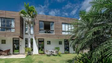 Un edificio de dos pisos con techo plano, ventanas amplias y un pequeño patio con mobiliario exterior.