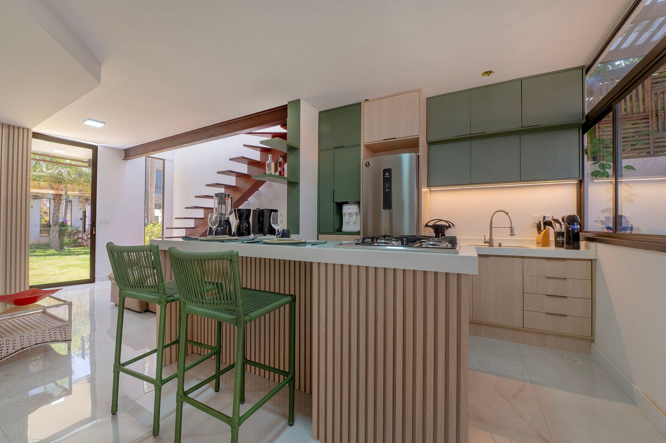 Cozinha moderna com ilha central, banquetas de bar e vista para o exterior.