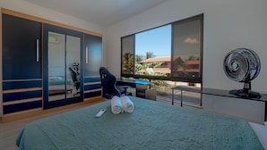 Un dormitorio moderno con una cama, un escritorio, una silla, un ventanal grande y un ventilador.
