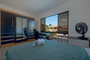 Ein modernes Schlafzimmer mit einem Bett, einem Schreibtisch, einem Stuhl, einem großen Fenster und einem Ventilator.