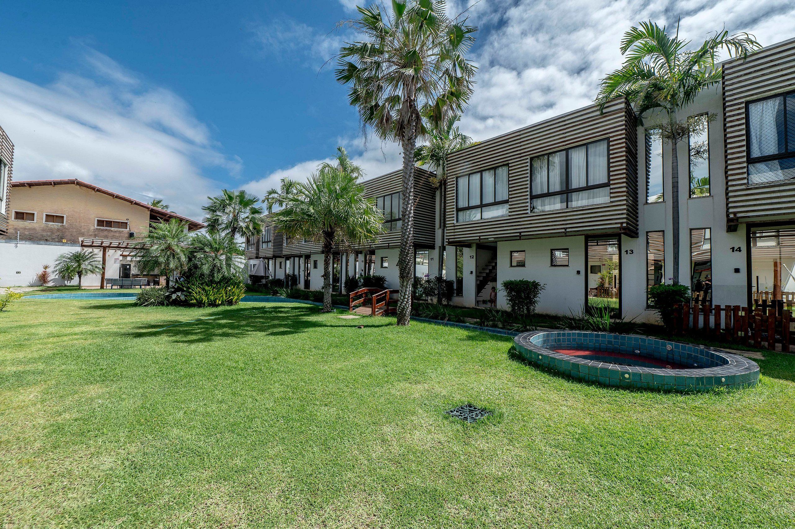 Un edificio residencial con piscina, palmeras y un césped bien cuidado.