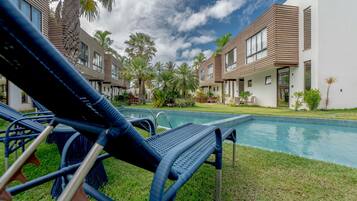 Un área moderna junto a la piscina con sillones de descanso, una piscina y una fila de edificios contemporáneos con grandes ventanales.